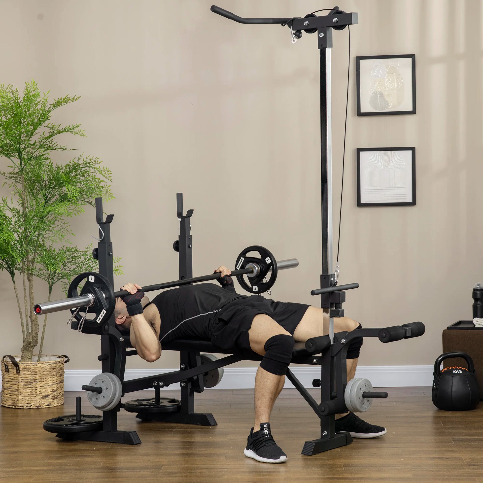 A person trains at home with the JB Muscle HOMCOM Multi Station Exercise Bench, lifting a barbell and using features like butterfly curl, lat pulldown, and leg curl on a wooden floor amid gym equipment.