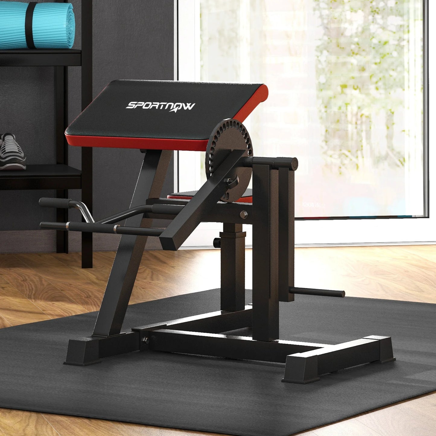 A JB Muscle SPORTNOW Adjustable Preacher Curl Bench, black and red with handlebar and elbow cushion, sits on a black mat in a room with wooden floors and a large window.