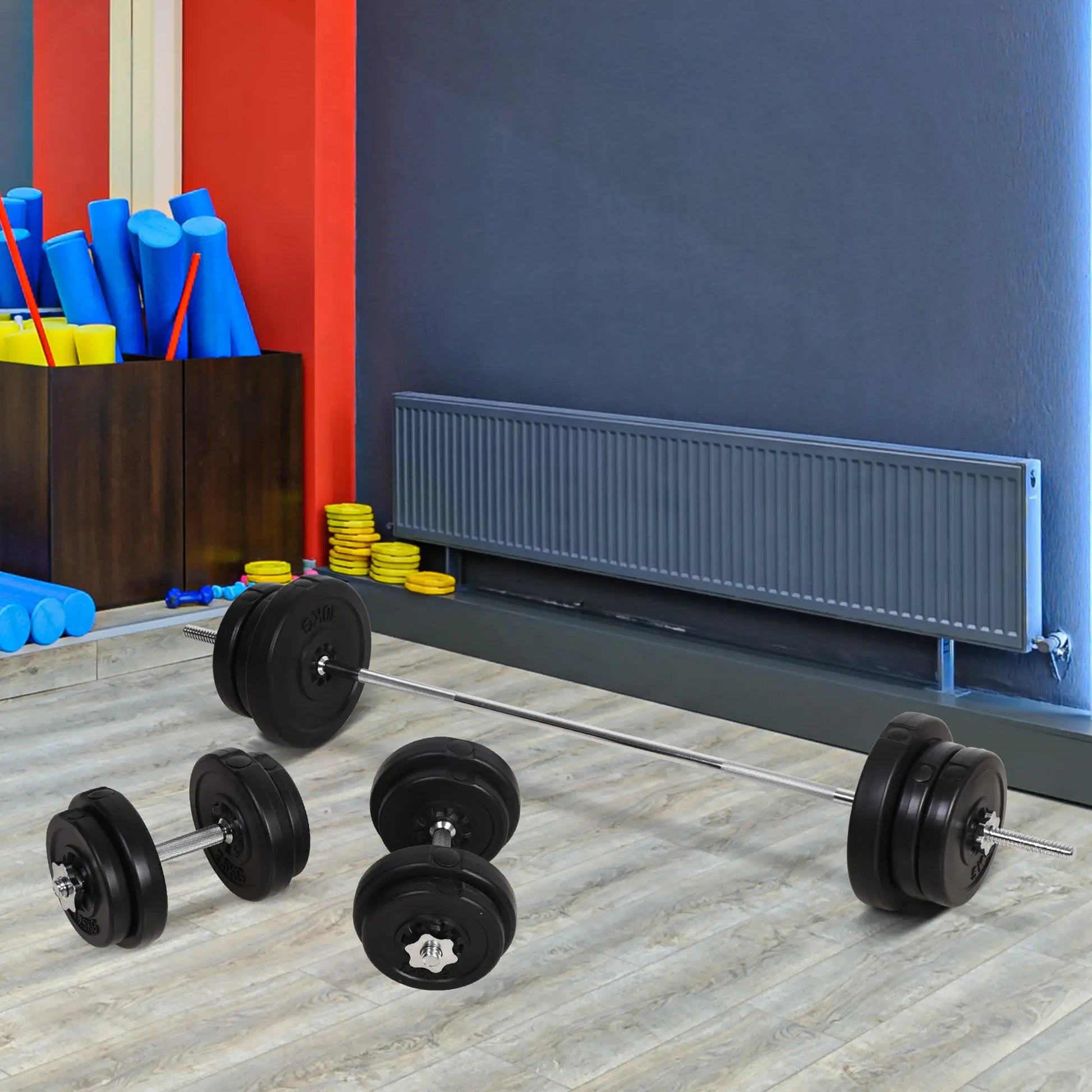 The JB Muscle Adjustable Dumbbell and Barbell Set 65kg rests on a light wood floor in a home gym, with foam rollers and yellow discs against a red and gray wall in the background.